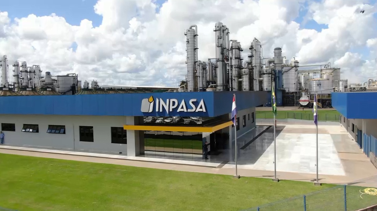 Fachada da fábrica da INPASA com torres industriais ao fundo e céu nublado
