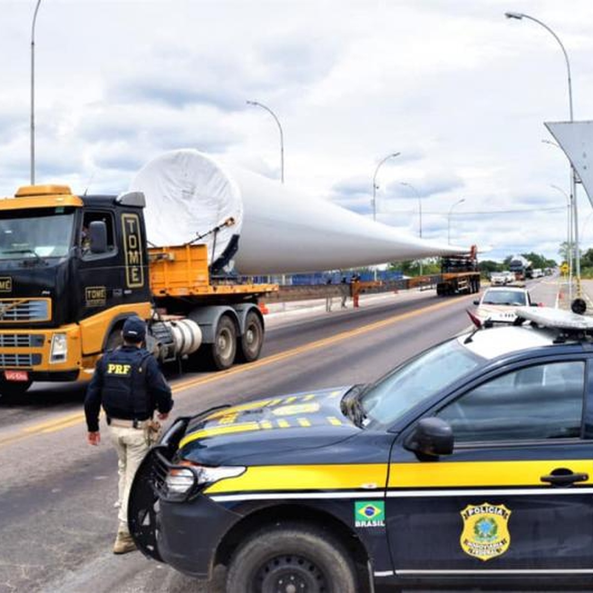 Caminhão transportando pá eólica escoltado pela Polícia Rodoviária Federal em rodovia brasileira