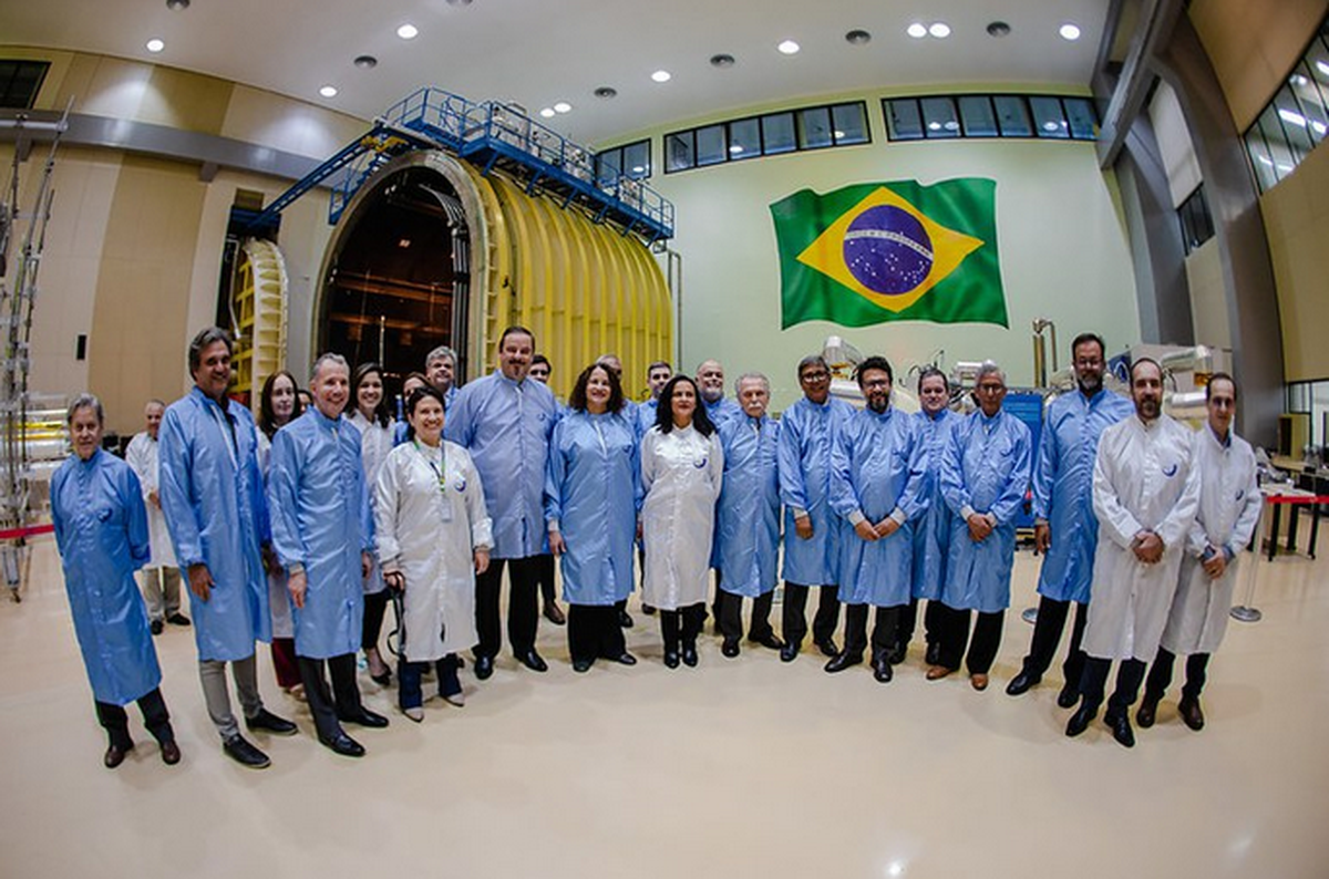 Autoridades brasileiras posam diante de módulo científico com bandeira do Brasil ao fundo em instalação de alta tecnologia.