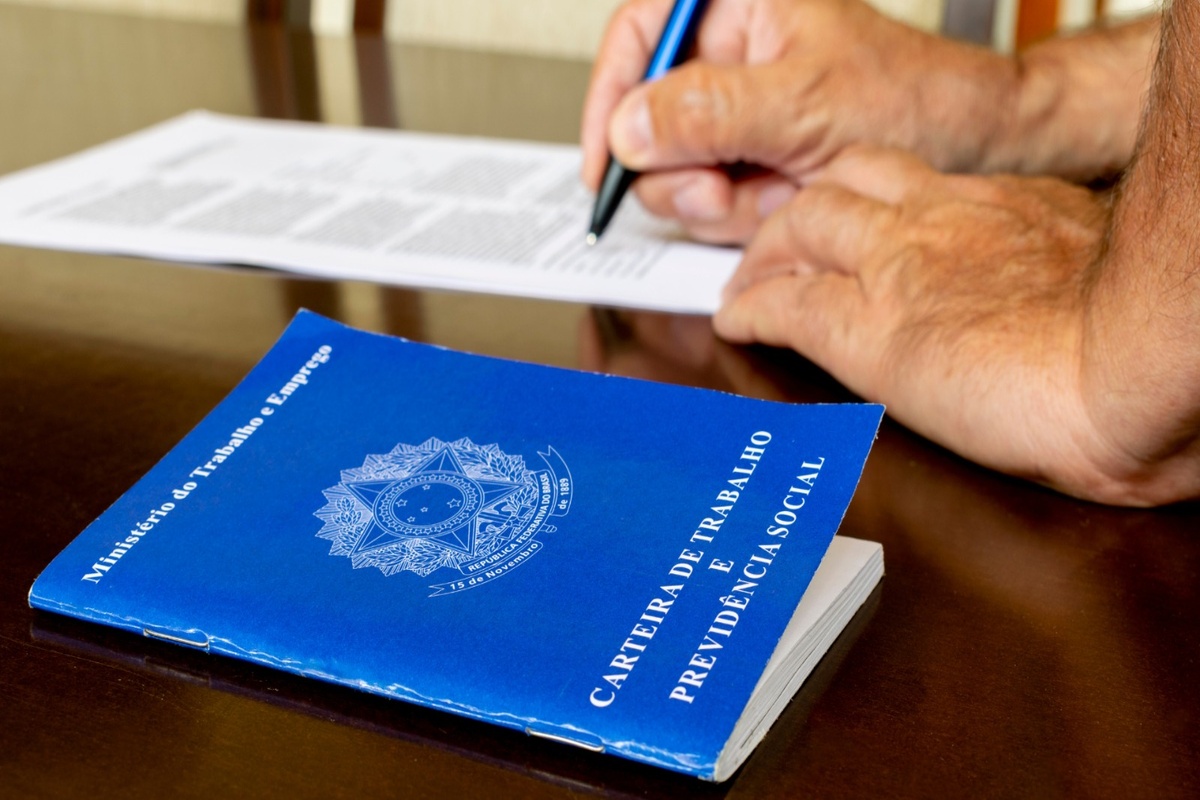 Carteira de Trabalho brasileira sobre mesa com pessoa assinando contrato