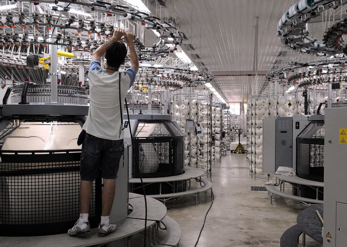 Operário ajustando máquina têxtil em fábrica de malharia industrial