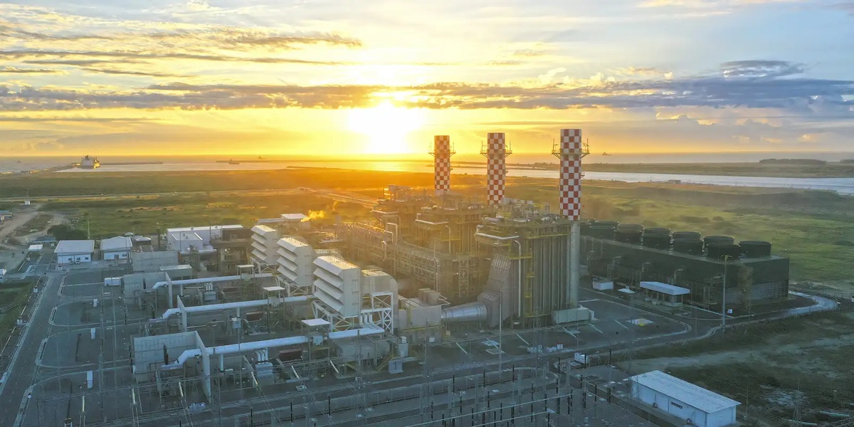 Unidade termelétrica GNA I vista aérea ao entardecer, com três torres de exaustão listradas ao fundo do mar.