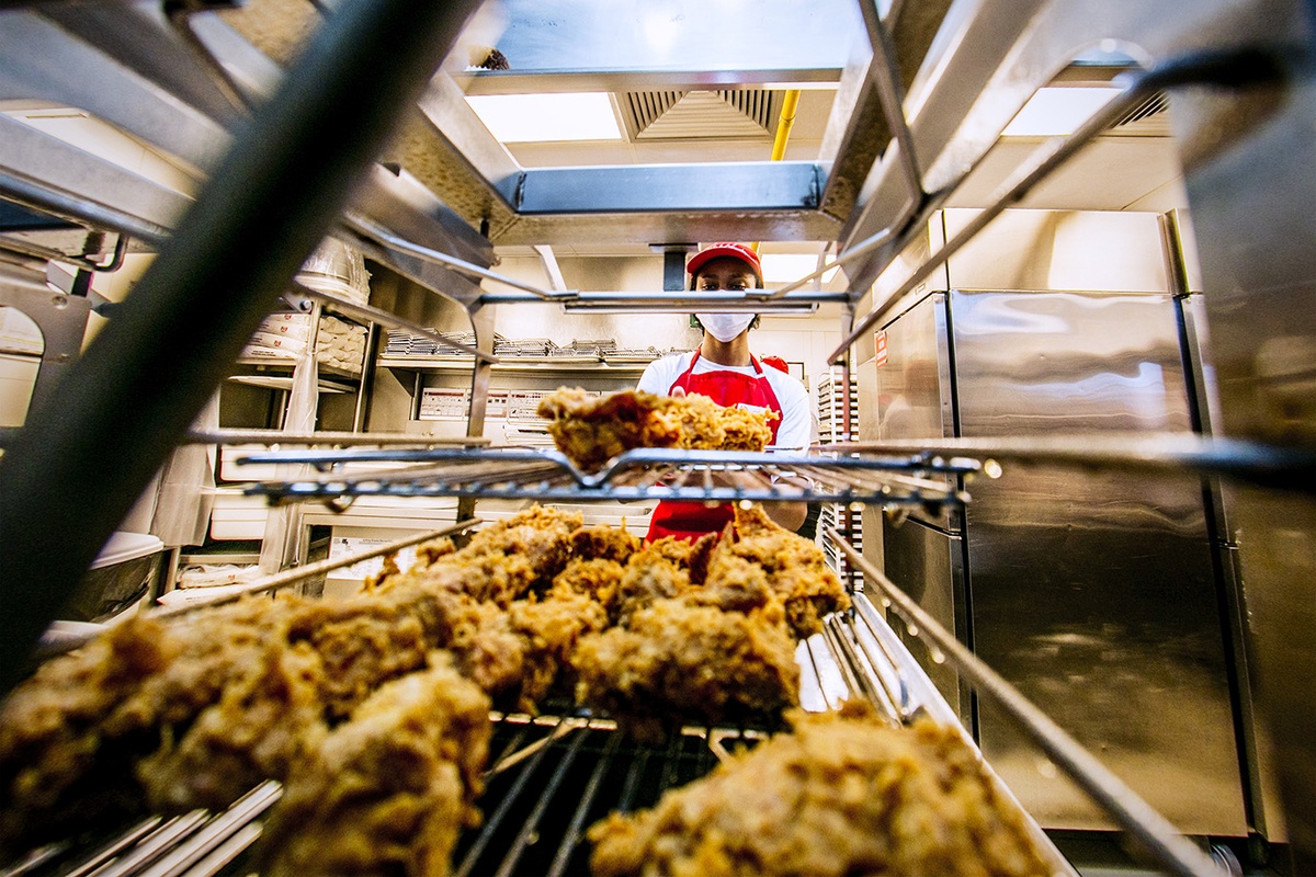 Funcionário organiza frango frito crocante em prateleiras de cozinha industrial