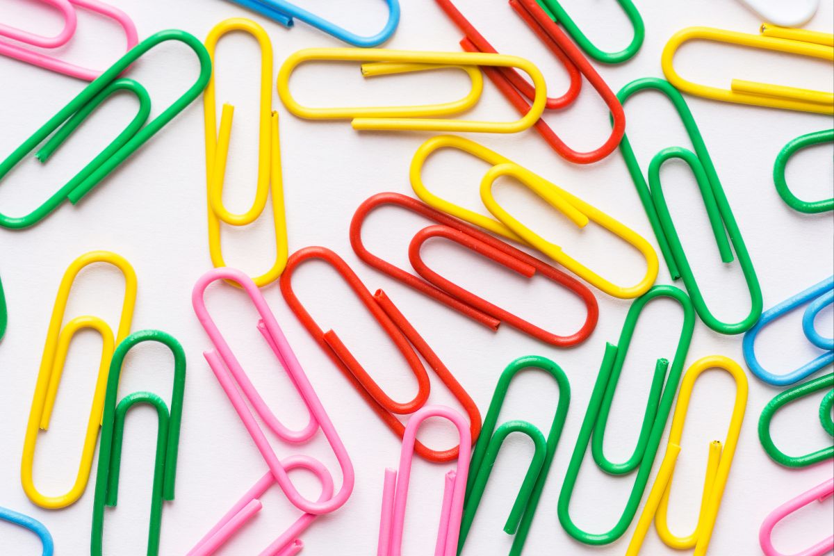 Uma vista de perto, de cima, de uma variedade vibrante de clipes de papel coloridos espalhados sobre uma superfície branca.