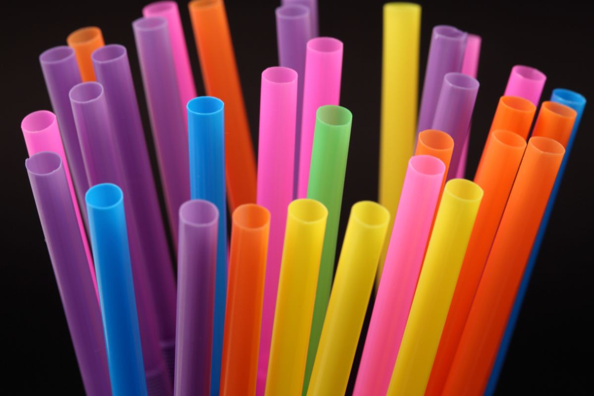 Uma variedade de canudos de plástico coloridos, com foco nas aberturas superiores, contra um fundo escuro.