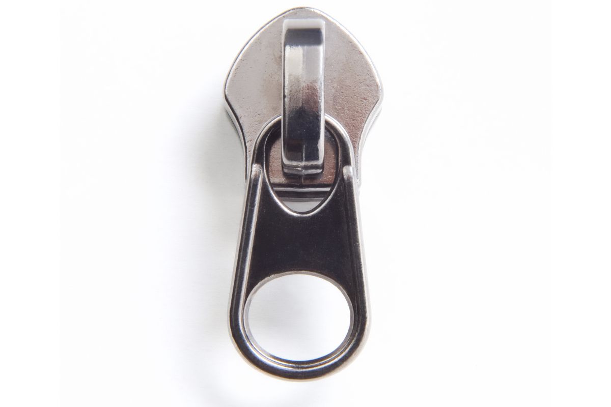 Puxador de zíper prateado escovado em close-up, centralizado em um fundo branco, destacando a textura e o design.