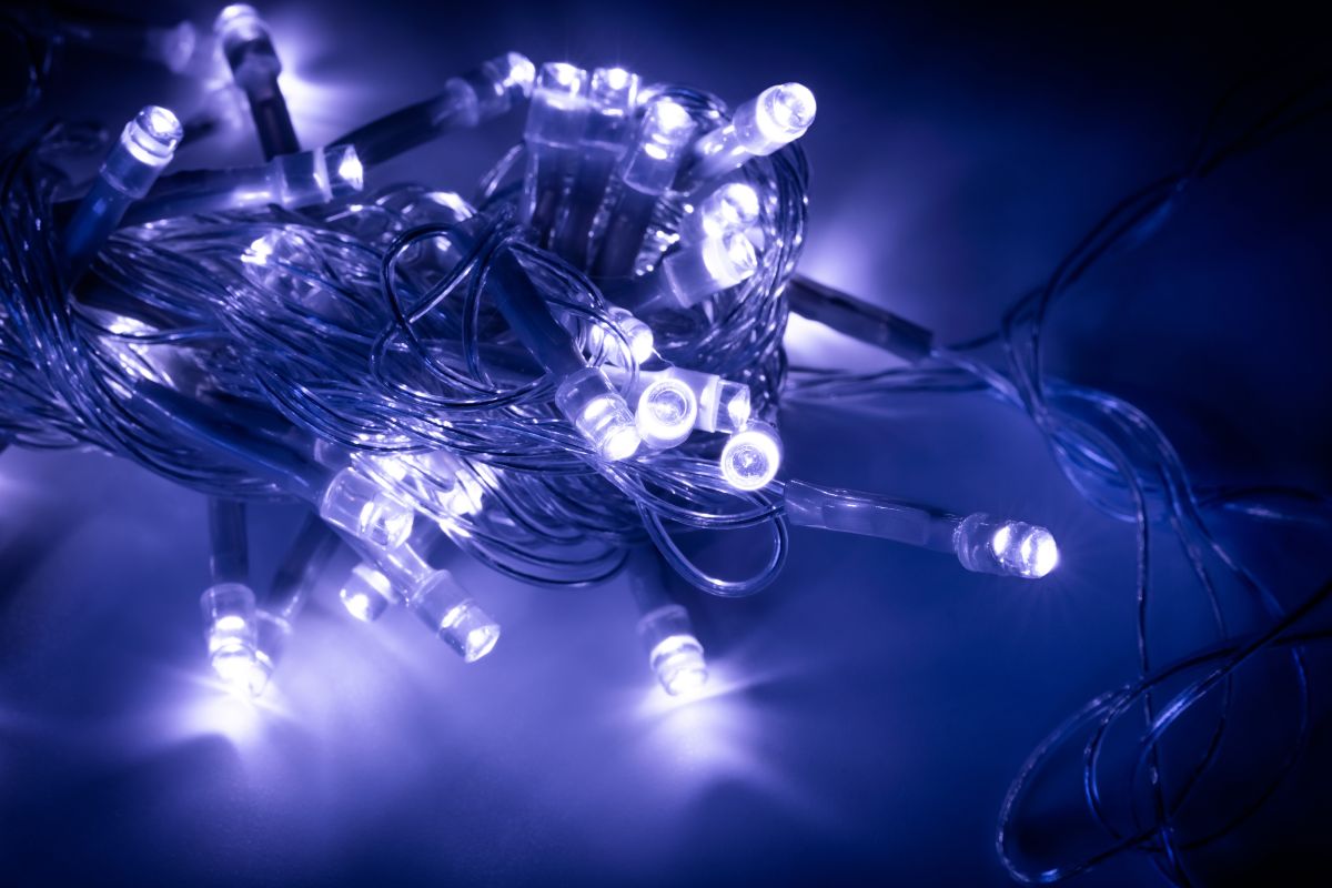 Cordão de luzes LED azuis e brancas emaranhado sobre superfície escura, demonstrando a versatilidade decorativa dos diodos emissores de luz