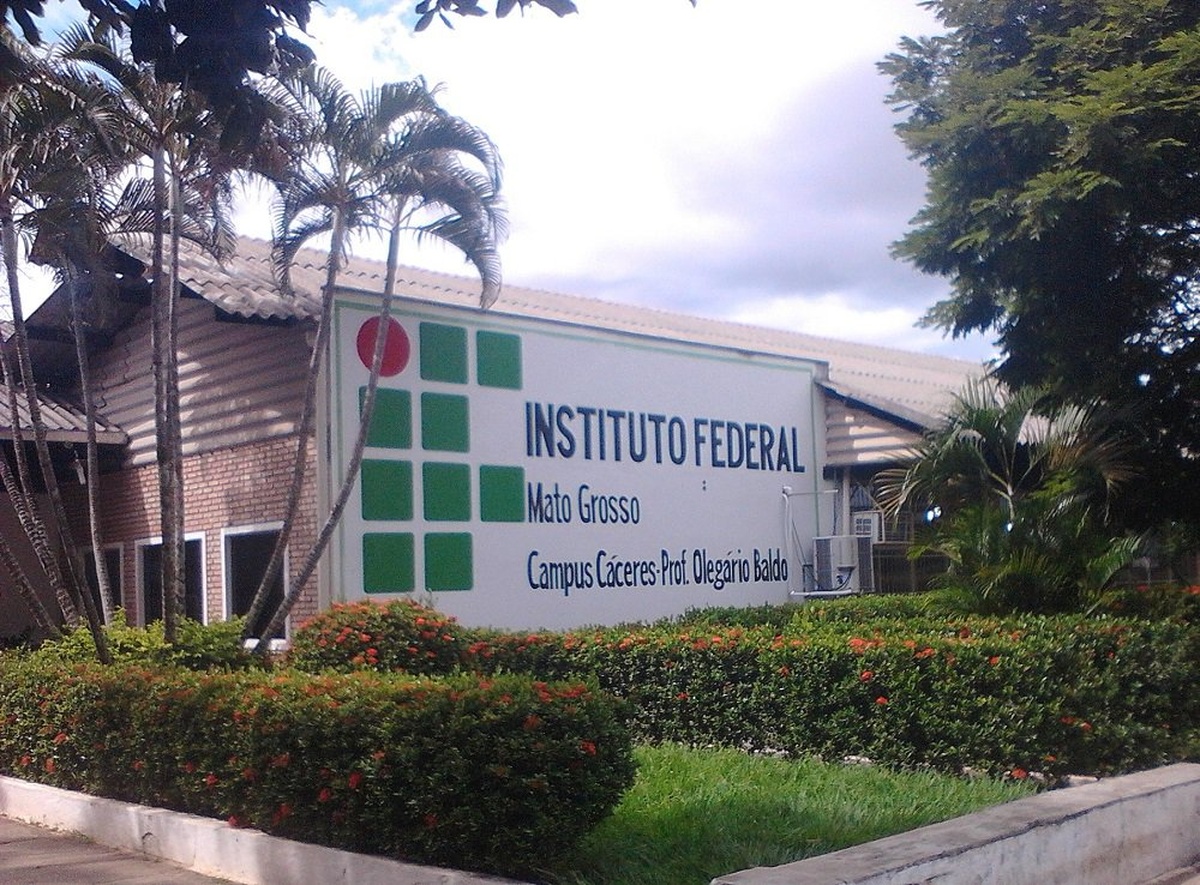 Fachada do Instituto Federal de Mato Grosso, Campus Cáceres, com jardim florido e céu parcialmente nublado.