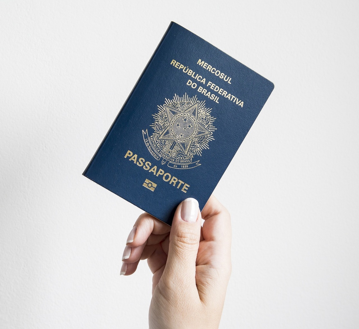 Mão segurando passaporte brasileiro azul com brasão da República