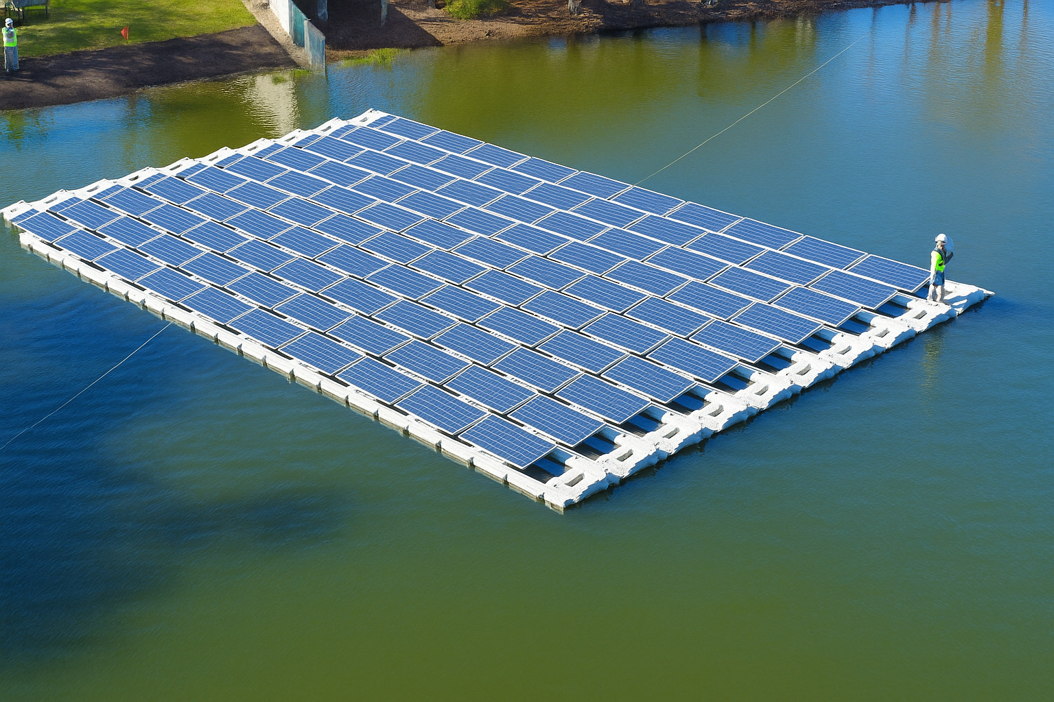 Sistema de painéis solares flutuantes em lago com água azul clara ao meio-dia