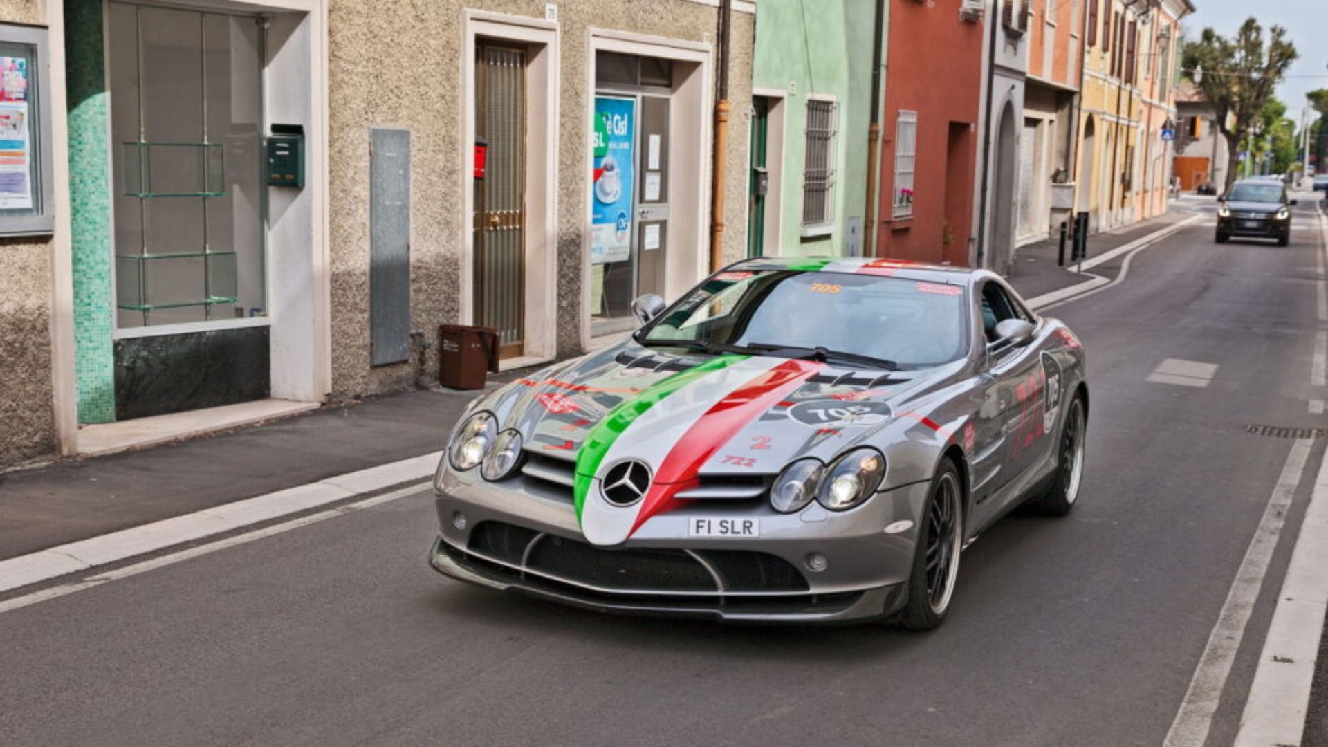 Supercarro Mercedes SLR McLaren com portas abertas, motor V8 visível e fundo de pista veloz sob céu nublado