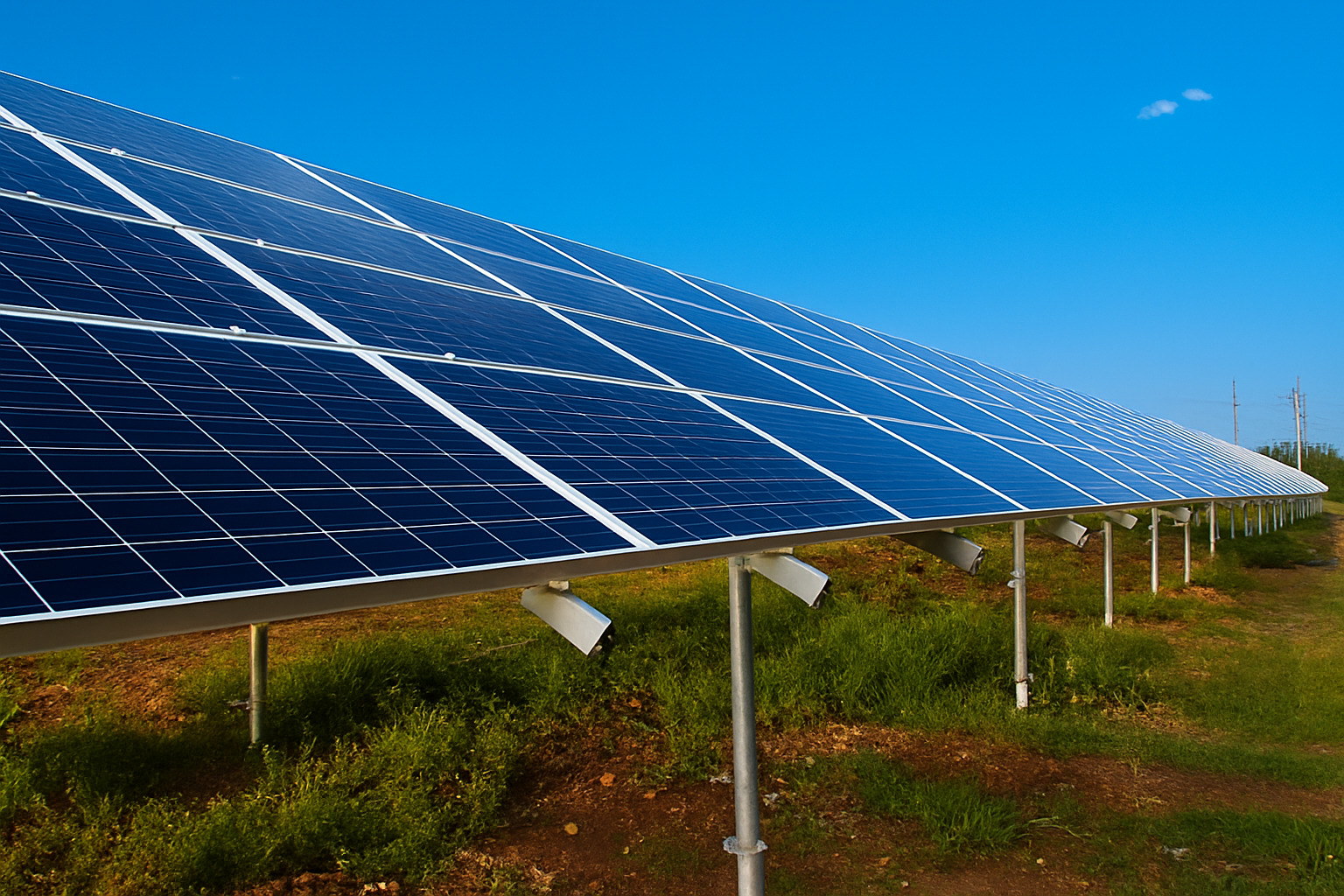 Painéis solares instalados em fileiras sobre solo com vegetação, sob um céu azul limpo.