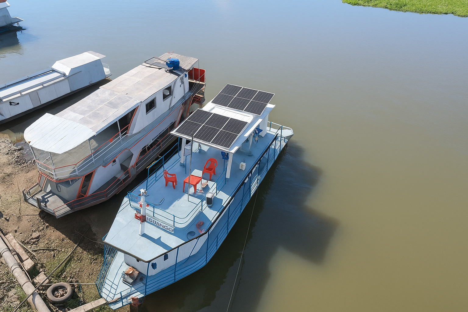 Barco equipado com painéis solares navegando em rio durante o meio-dia.