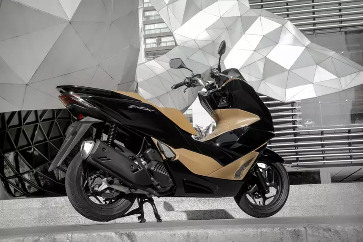 Scooter Honda PCX 160 2026 em preto e dourado, estacionada em área urbana com arquitetura moderna ao fundo