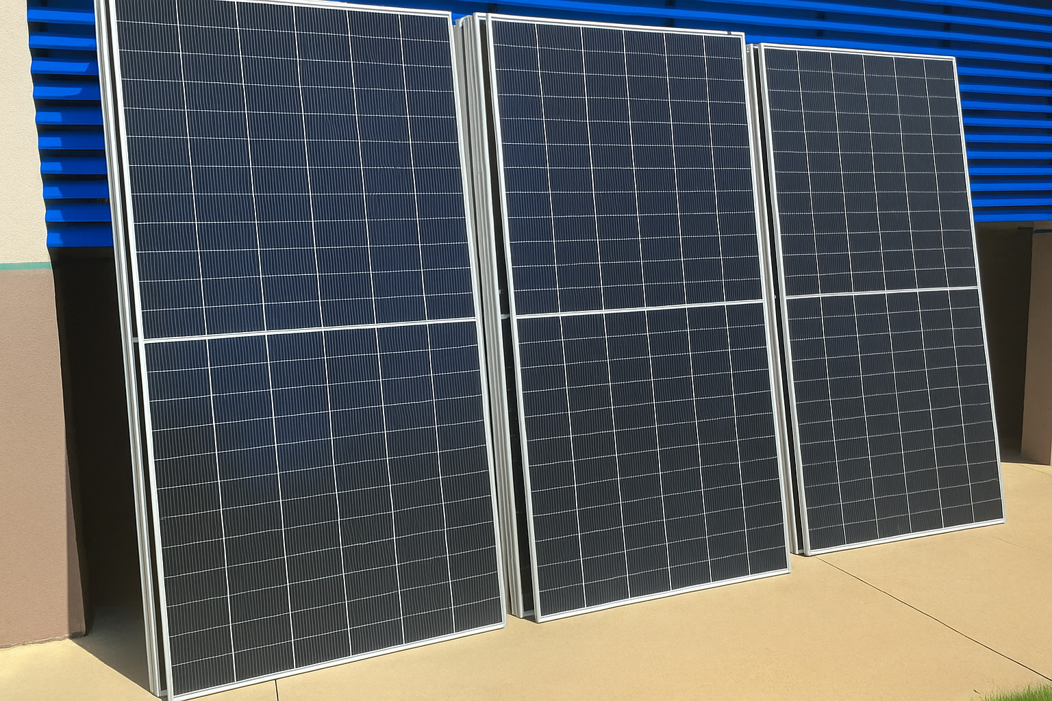 Três painéis solares apoiados em parede com barras azuis