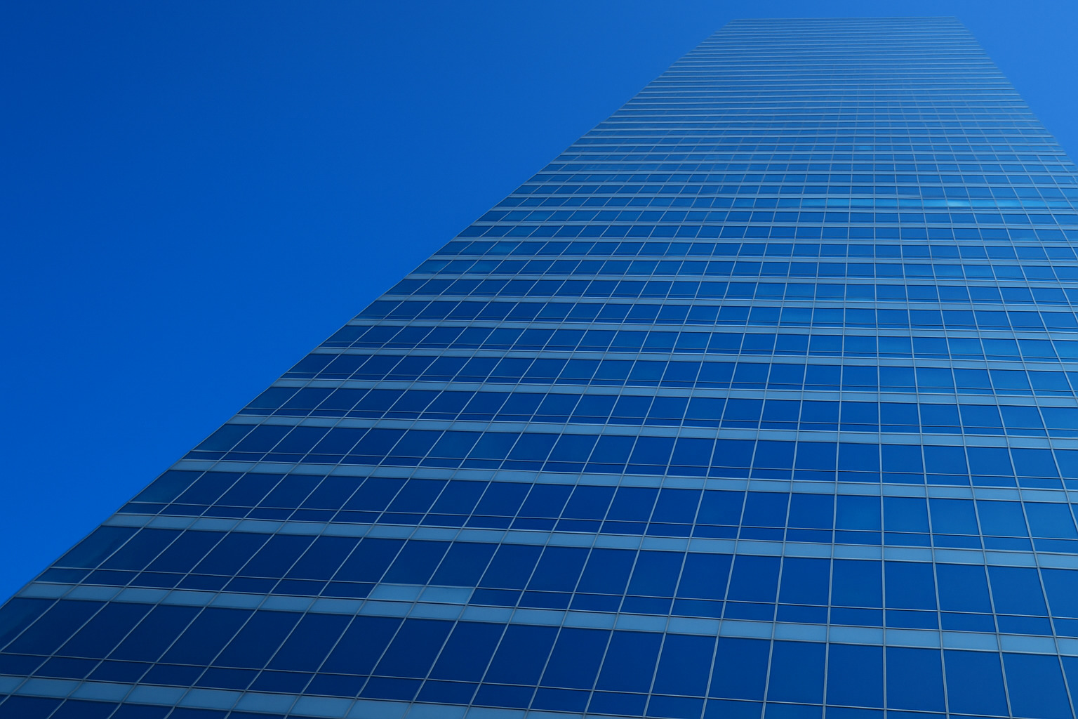 Arranha-céu moderno com fachada de vidro refletindo o céu azul limpo.