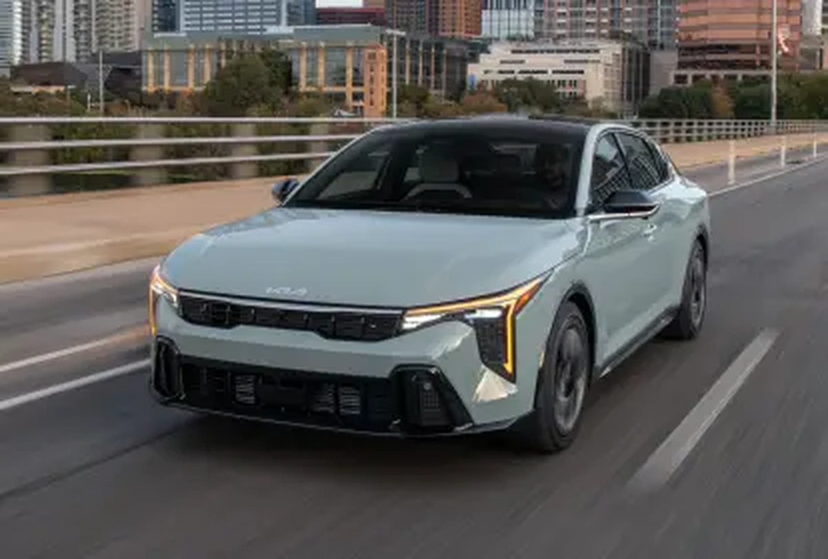 Kia K4 GT-Line em movimento sobre uma ponte urbana com prédios ao fundo
