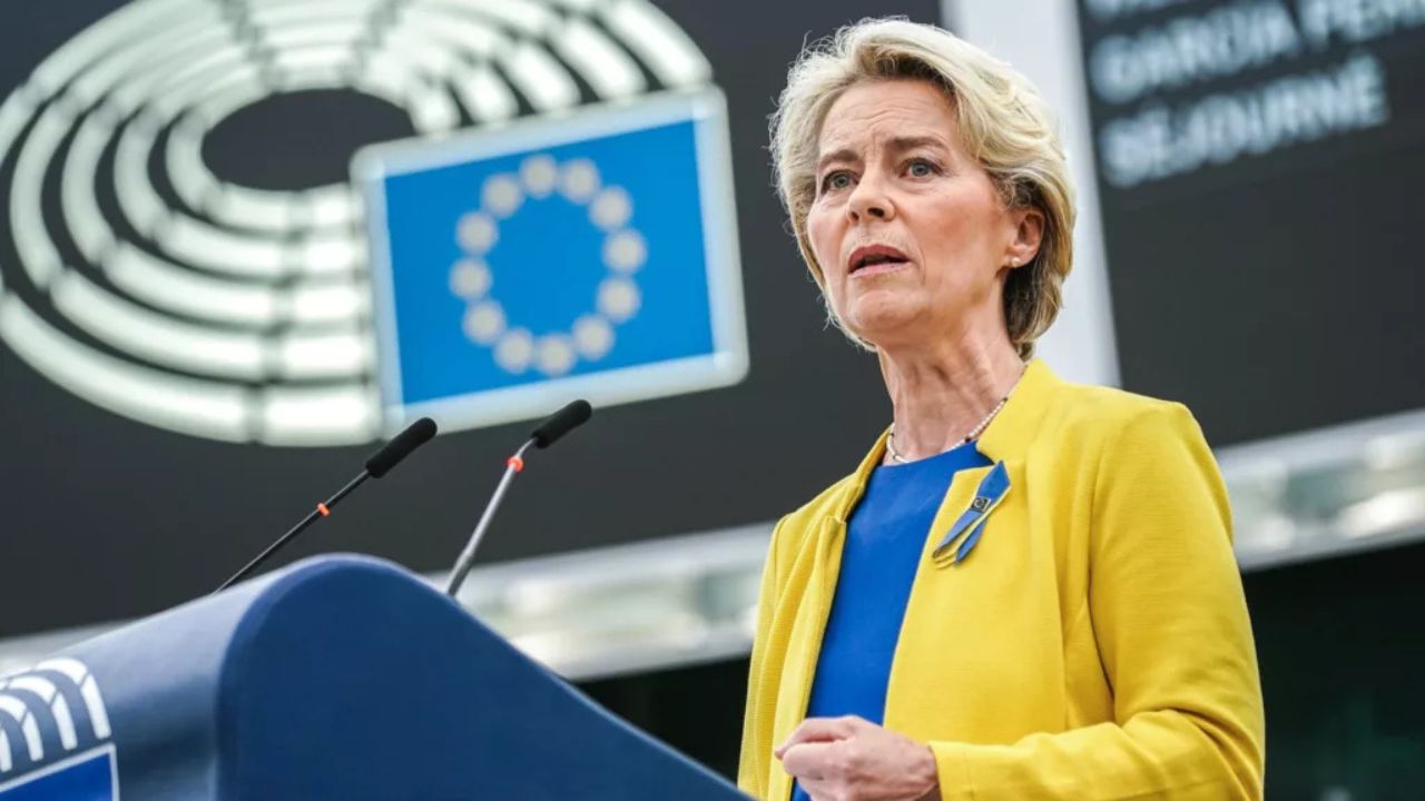 Ursula von der Leyen discursando em um púlpito diante do emblema da União Europeia, em ambiente institucional.