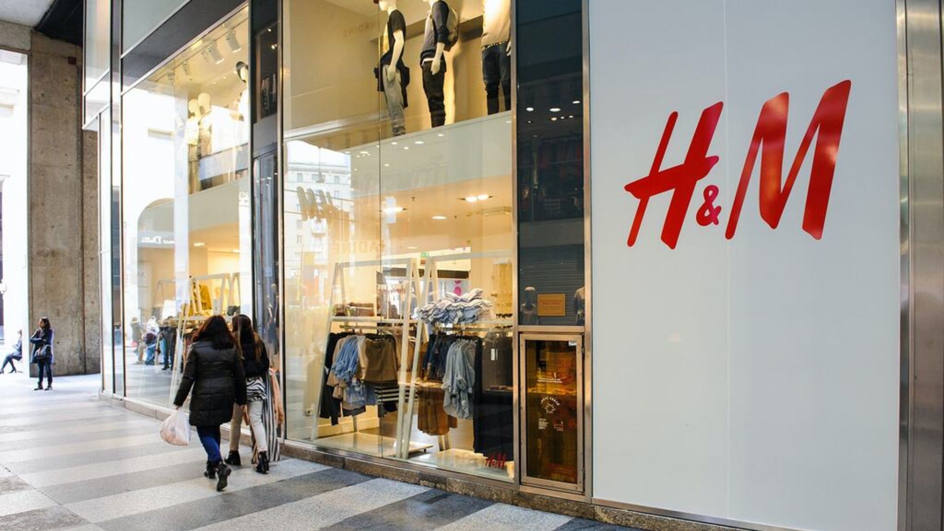 Fachada iluminada da H&M em shopping brasileiro com clientes entrando.
