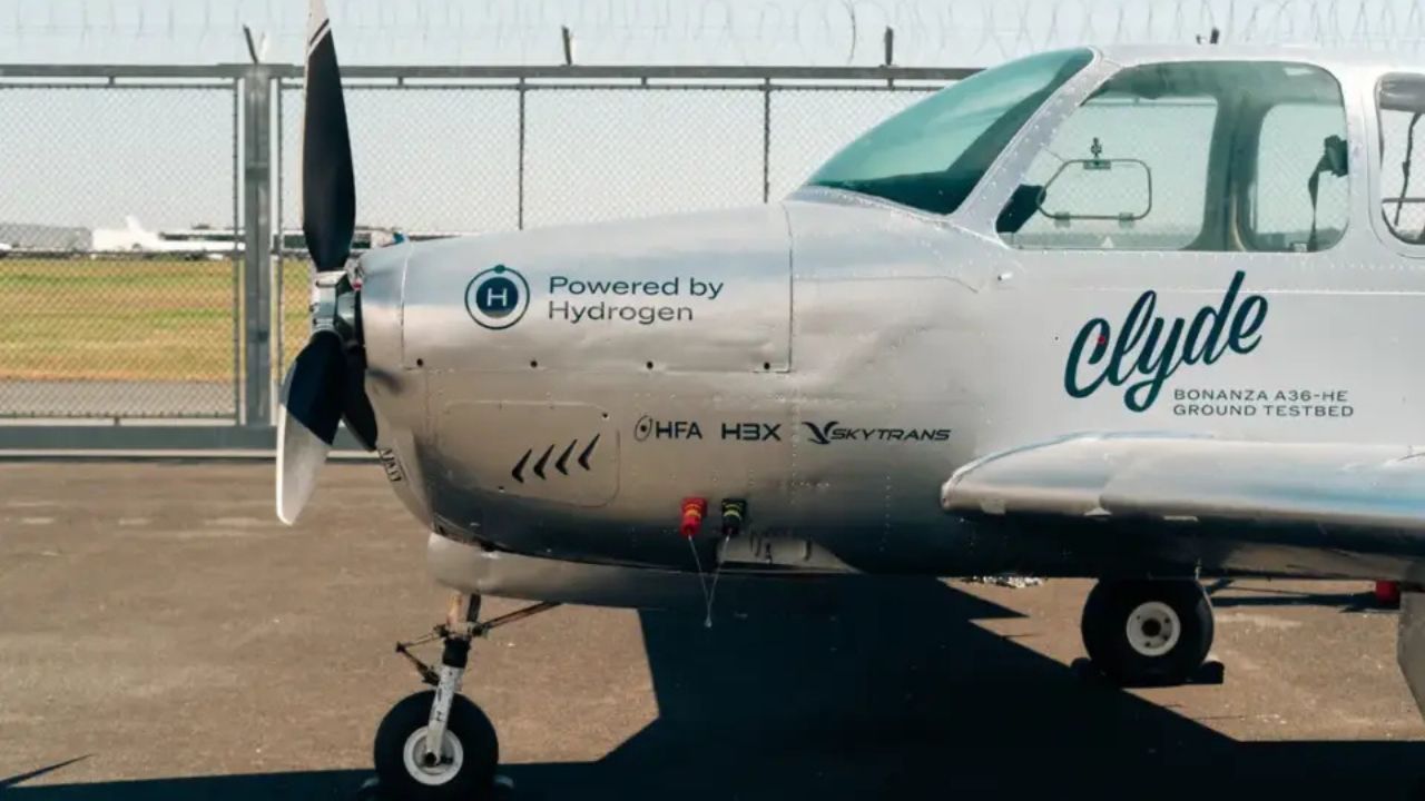 Avião experimental Bonanza A36 movido a hidrogênio estacionado em pista de testes, com logotipos de empresas parceiras e símbolo H₂ visível na fuselagem.