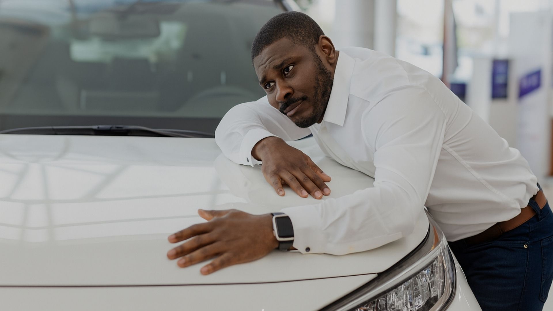 Homem abraçando um carro com expressão preocupada dentro de concessionária, simbolizando a dificuldade de financiar um veículo no Brasil com a taxa Selic em 15%, juros altos e crédito caro.