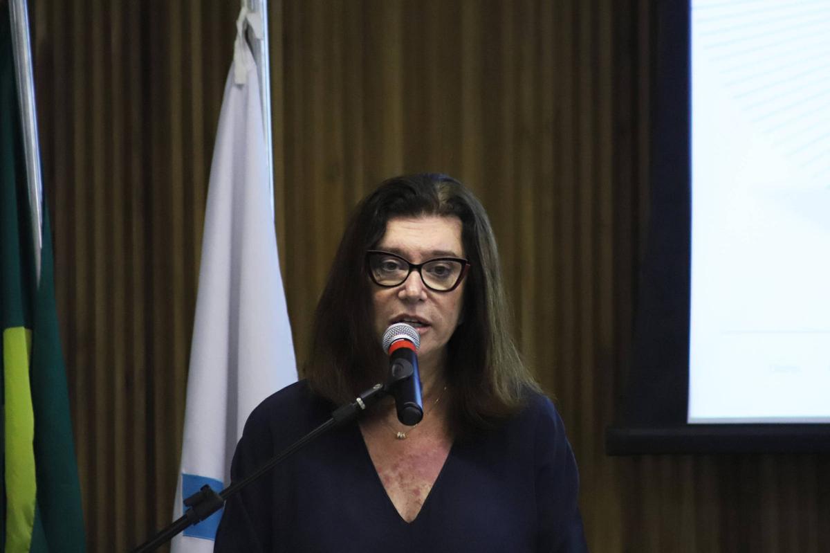 Presidente da Petrobras fala ao público durante evento oficial, com bandeiras e apresentação institucional ao fundo.