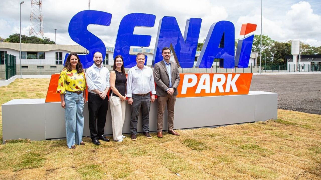 Cinco pessoas em frente ao letreiro colorido “SENAI PARK” durante cerimônia de inauguração em Suape, Pernambuco.
