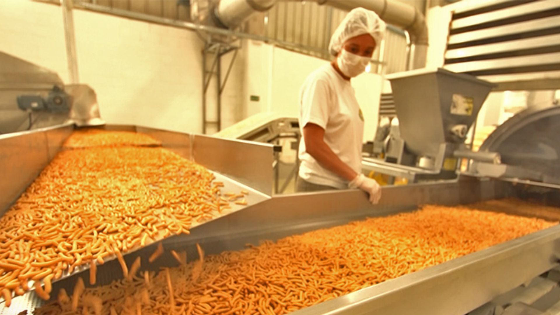 Produção de salgadinhos Lobits na fábrica da Milho de Ouro, com maquinário industrial e equipe uniformizada.