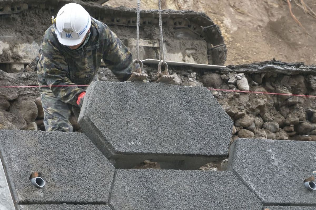 Três engenheiros japoneses conduzem um projeto de recuperação que utiliza blocos de concreto e fôrma de concreto reforçada, com base em camadas de pedra britada. O trabalho mostra o avanço técnico e a precisão das obras de reconstrução nas áreas afetadas, em um raro registro do Japão pós-desastre.