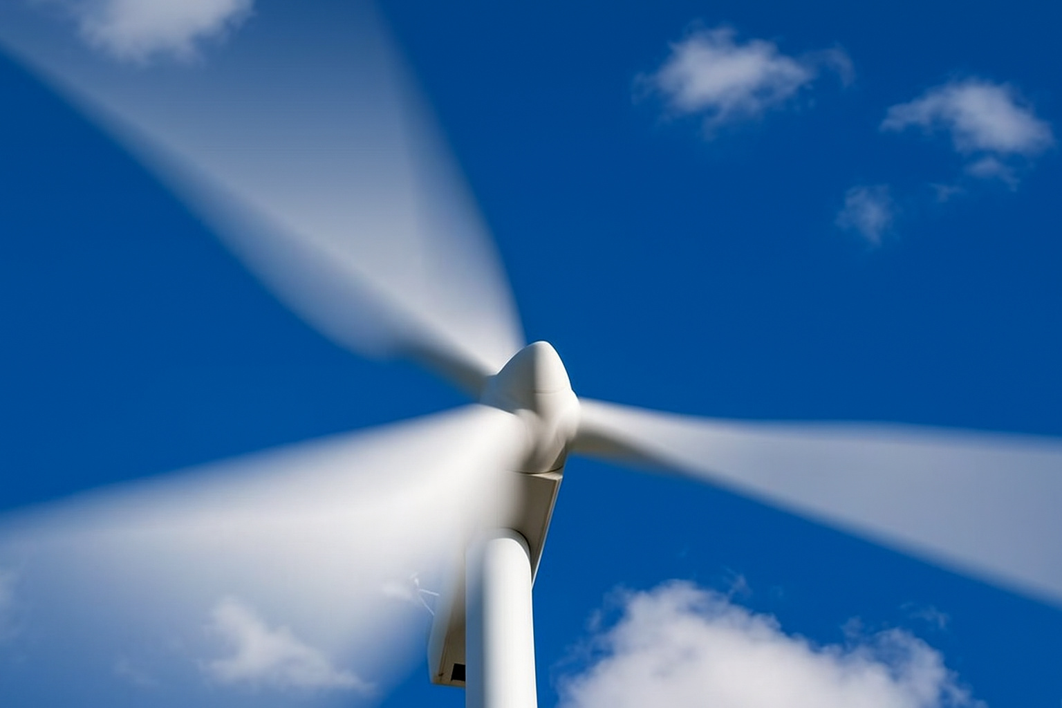Turbina eólica em movimento sob céu azul com algumas nuvens dispersas.