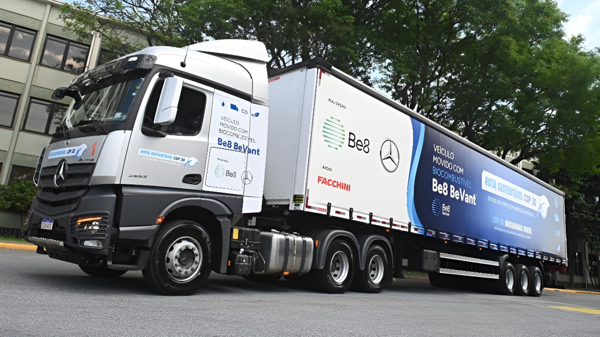 Caminhão Mercedes-Benz movido 100% por biodiesel BeVant da Be8, estacionado em frente a prédio urbano com árvores ao fundo.