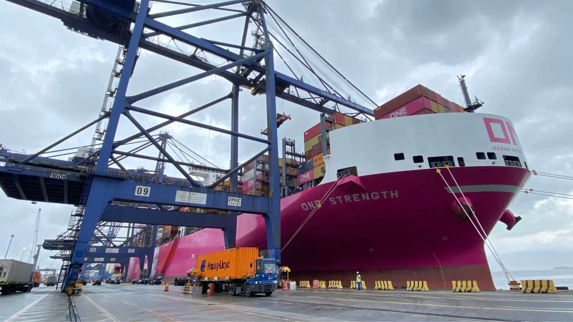 Navio porta-contêineres ONE Strength atracado no Terminal de Contêineres de Paranaguá durante operação de carga, com guindastes azuis e caminhões no cais