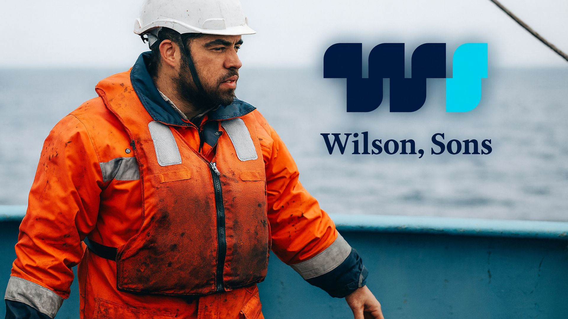 Trabalhador marítimo com colete de segurança e capacete branco em embarcação da Wilson Sons, com o oceano ao fundo
