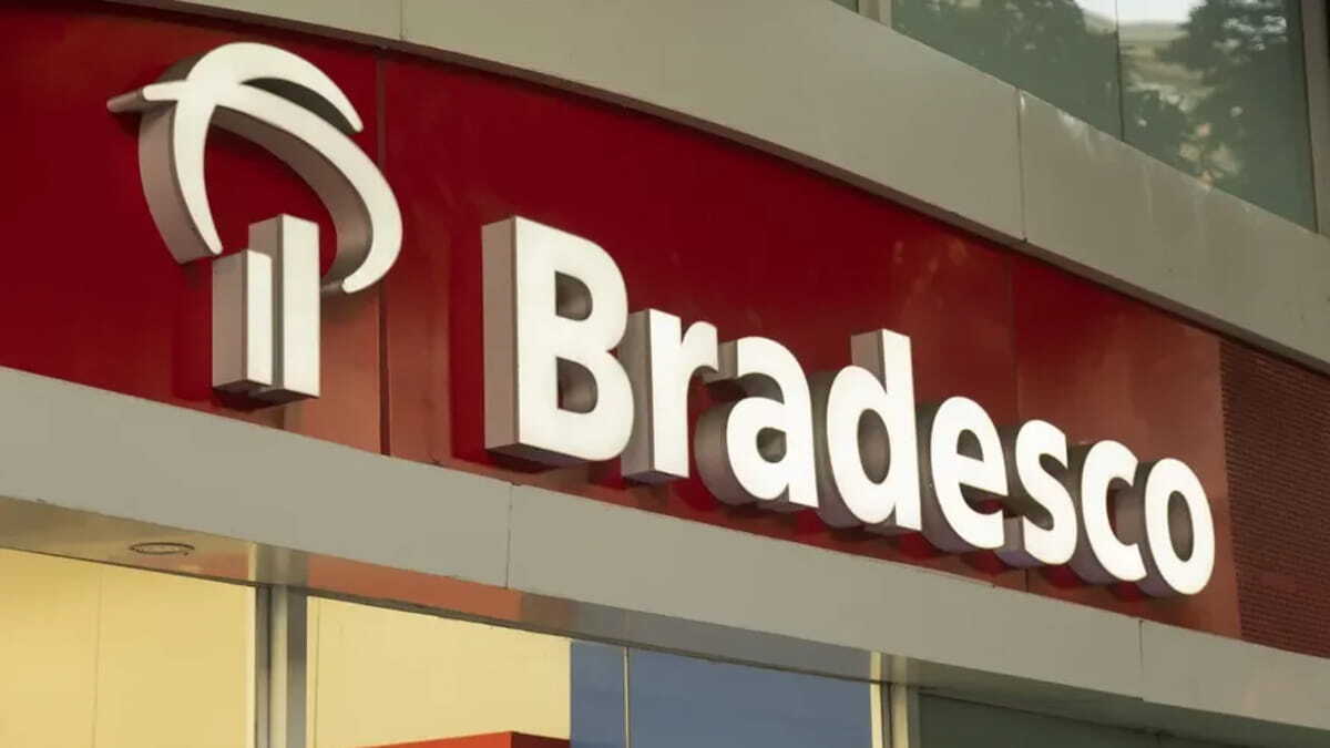 Fachada do Bradesco com logotipo iluminado e aviso em amarelo sobre anúncio de centenas de vagas de emprego.