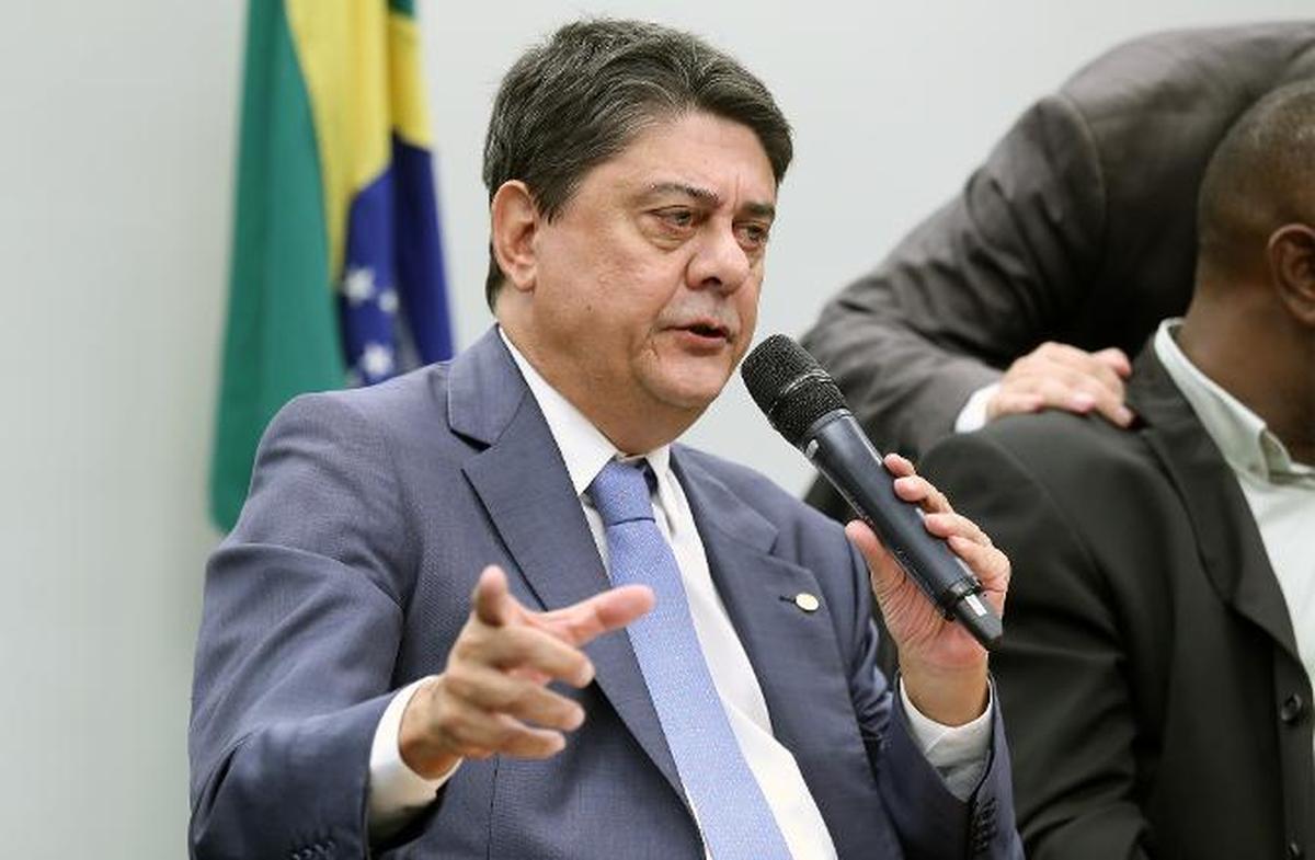 Dirigente em evento oficial segurando um microfone durante debate público sobre regras de planos de saúde no Brasil.