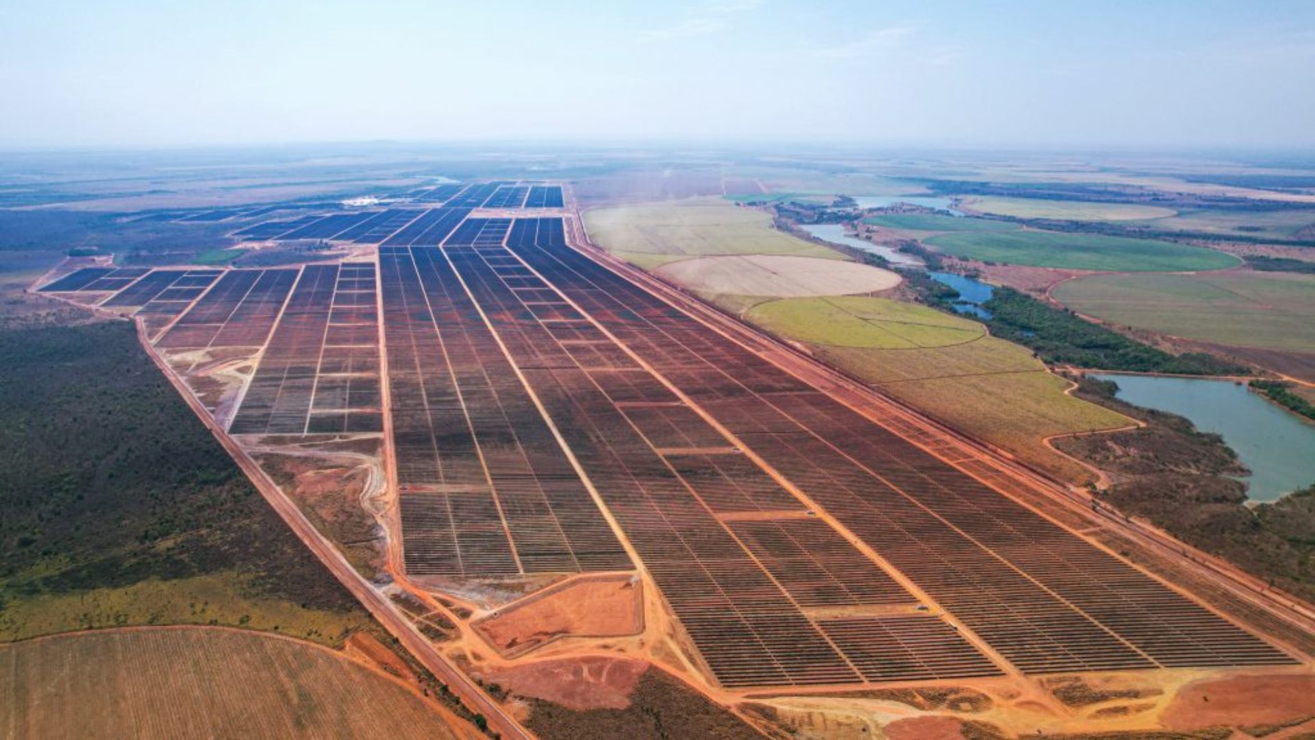 Vista aérea de um grande parque solar em Minas Gerais, com fileiras extensas de painéis fotovoltaicos distribuídos em ampla área rural.