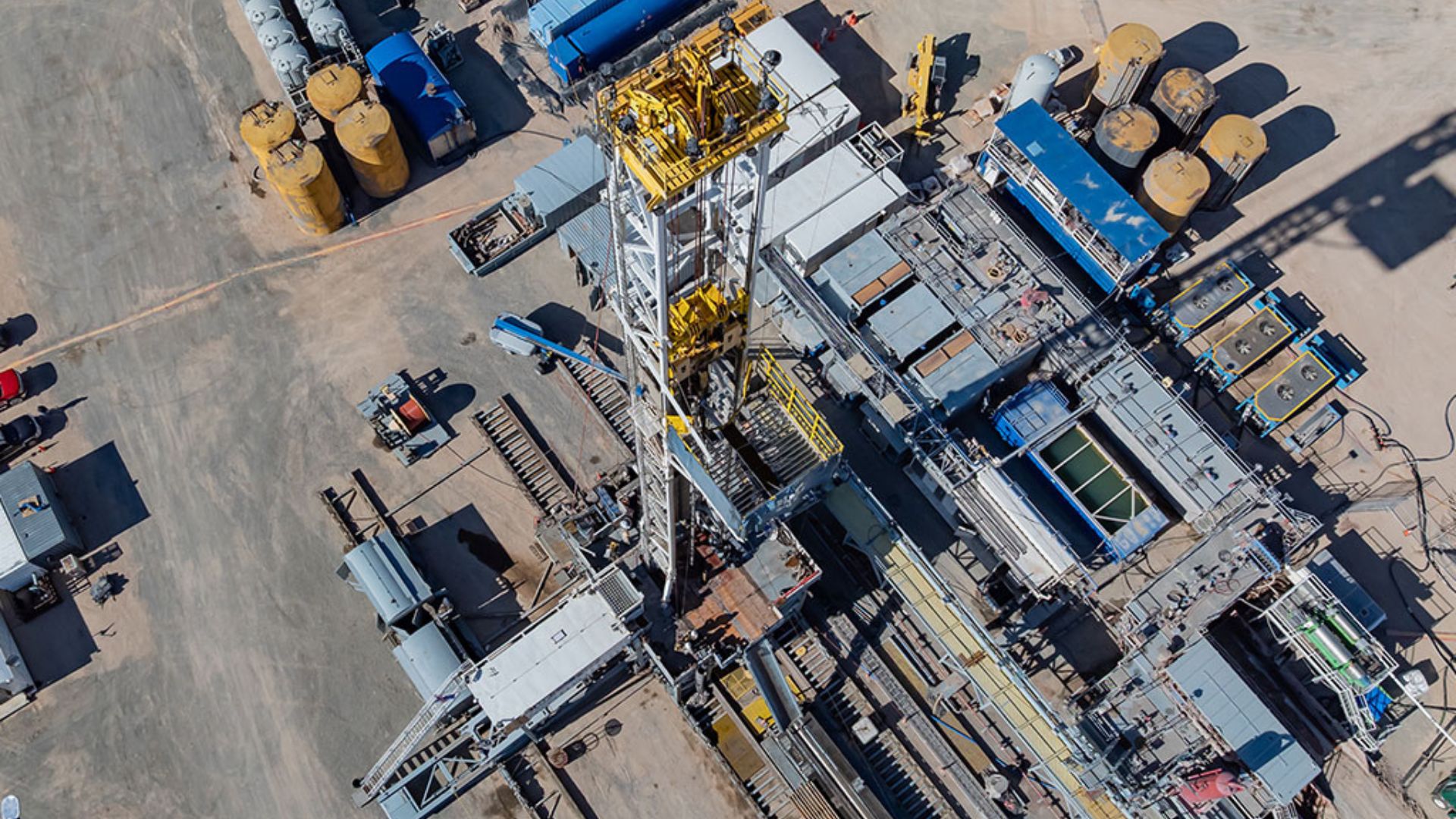 Plataforma industrial vista de cima com torre de perfuração e estruturas operacionais em área de exploração geotérmica.