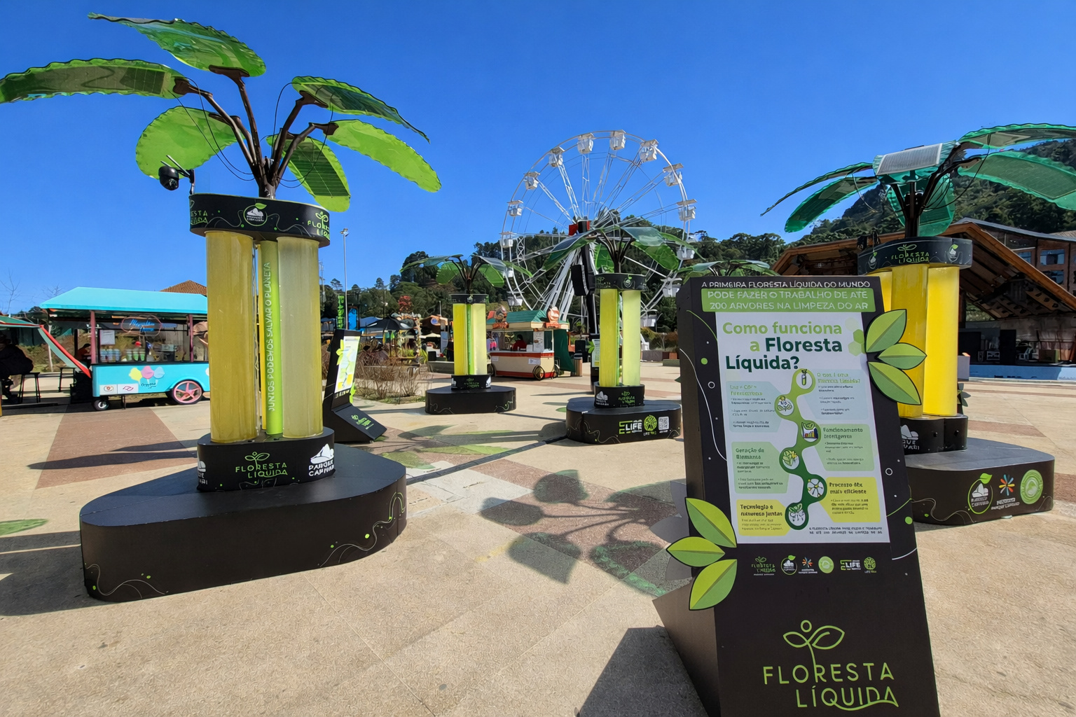 Instalação Floresta Líquida no Parque Capivari, com estruturas verdes e roda-gigante ao fundo sob céu azul limpo.