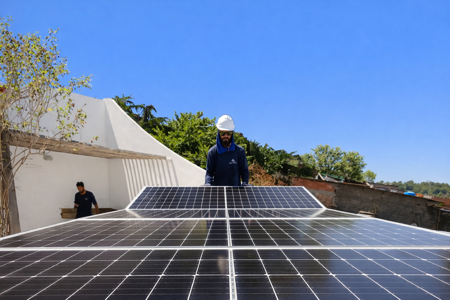 Técnicos instalando painéis solares em telhado residencial em dia ensolarado, com céu azul limpo e vegetação ao redor.