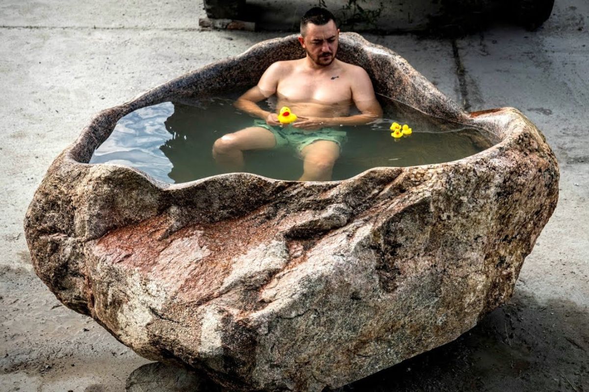 A banheira de pedra esculpida à mão a partir de granito e de uma rocha de 23.000 libras consumiu meses, muitos disco de corte e polimento e uma rotina intensa contra poeira, riscos e lesões em oficina ao ar livre.