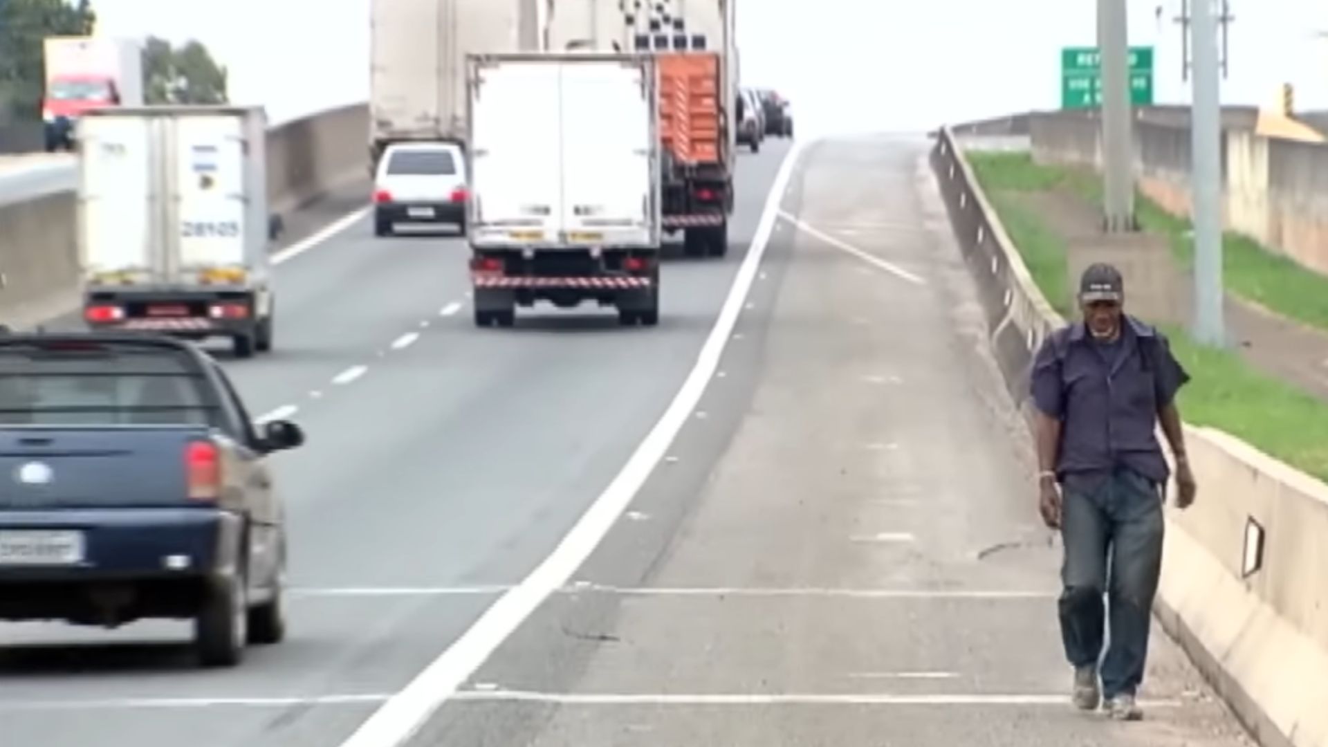 Andarilho caminhando sozinho por rodovia brasileira sob sol forte com mochila nas costas.