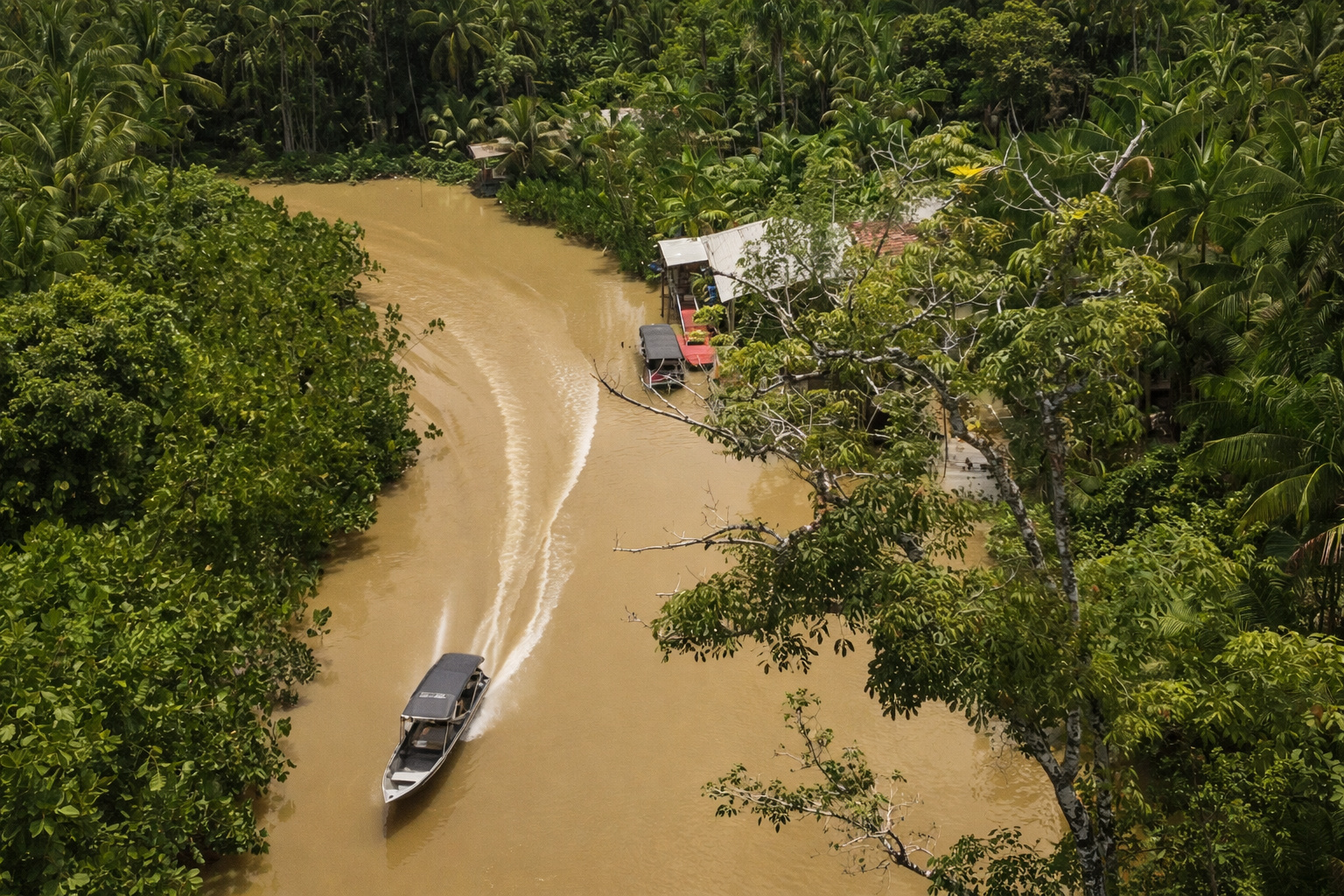 Vista aérea de rio amazônico com embarcação navegando entre áreas verdes, ilustrando calor intenso, vegetação reduzida e impactos ambientais no cotidiano urbano.