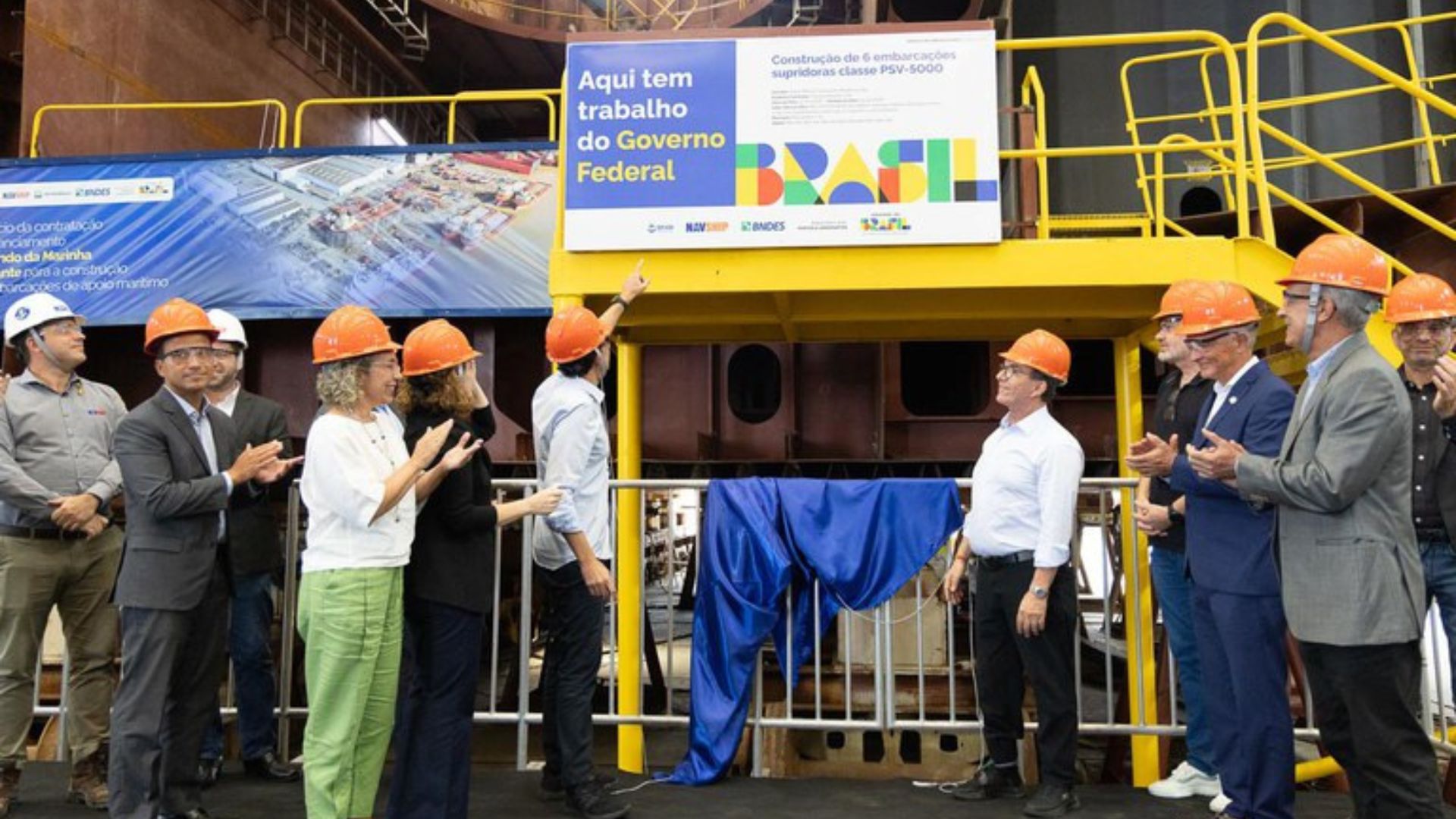 Autoridades e trabalhadores com capacetes laranja participam de cerimônia em estaleiro, diante de plataforma amarela com placa do Governo Federal anunciando a construção de seis embarcações supridoras classe PSV-5000 em Santa Catarina.