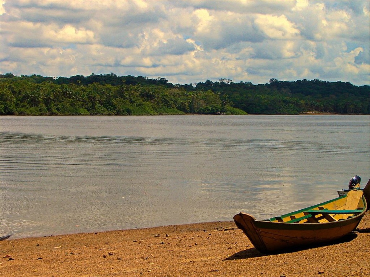 Rio amazônico no Amapá com barco tradicional na margem, em área próxima à Margem Equatorial onde a exploração de petróleo pode gerar royalties e transformar a economia local.
