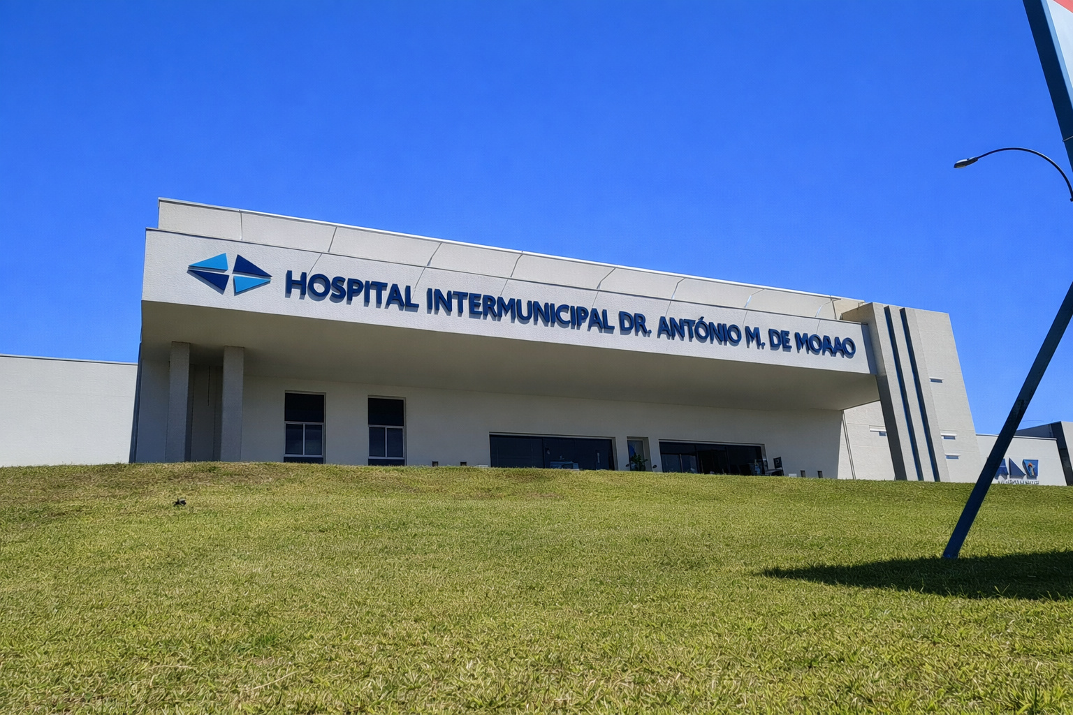 Fachada do hospital em dia ensolarado, com gramado em primeiro plano e céu azul limpo ao fundo.