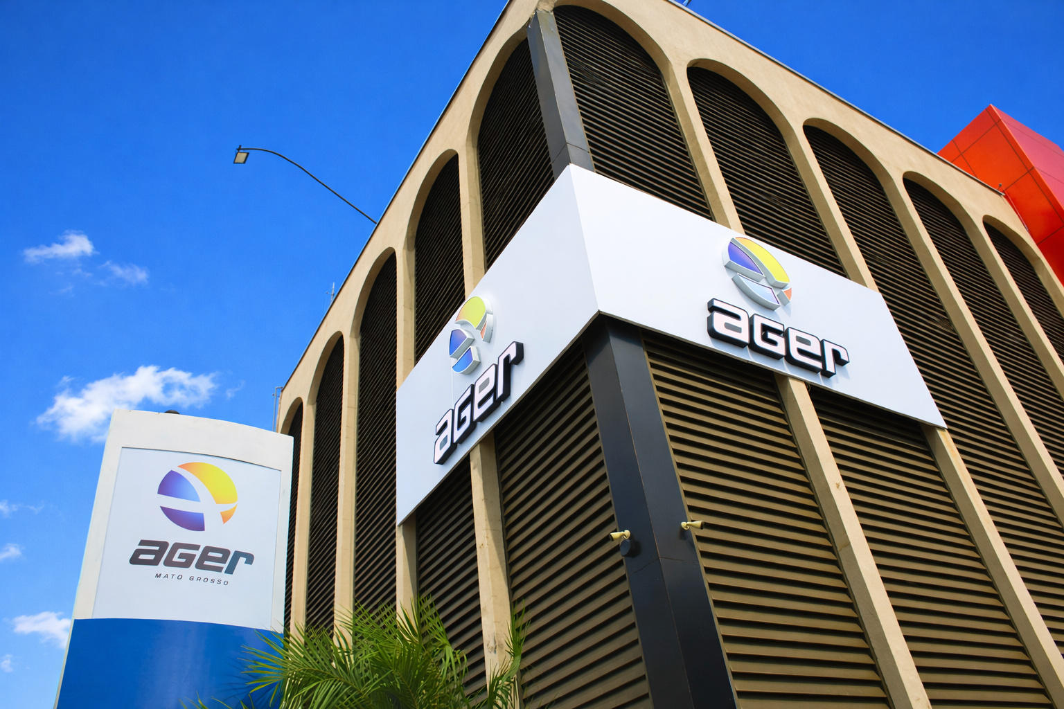 Texto alt: Fachada moderna do prédio da Ager-MT com logotipo em destaque, sob céu azul, em Mato Grosso.