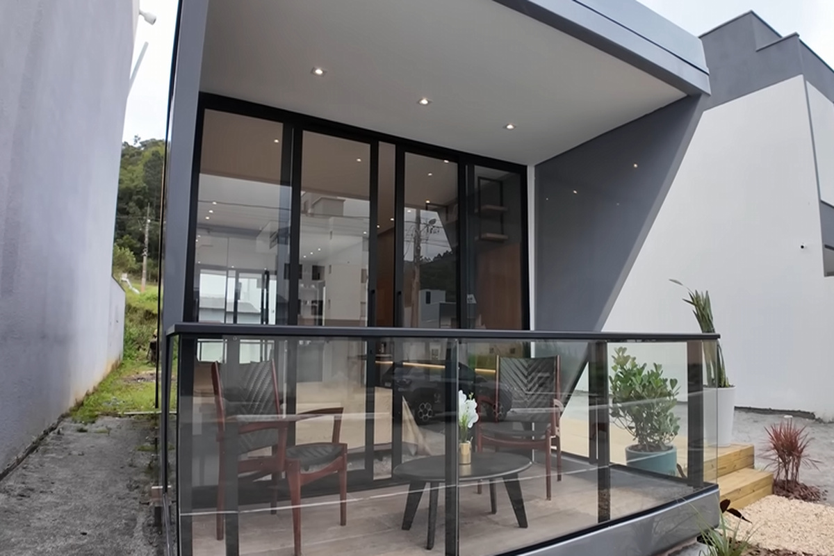 Casa cápsula em fibra náutica com varanda de vidro, porta de correr ampla e acabamento moderno instalada em terreno urbano.