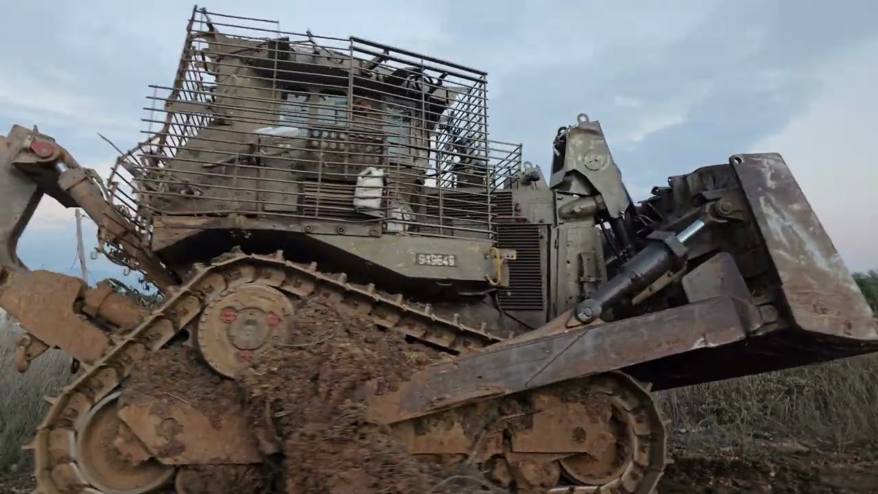 Conheça o trator blindado de 70 toneladas que derruba prédios e resiste a foguetes: o D9 israelense que carrega 15 toneladas de blindagem adicional para arrastar 4 andares de concreto em minutos, sobreviver a RPG direto na cabine e abrir caminho para tropas no meio de zona de guerra urbana