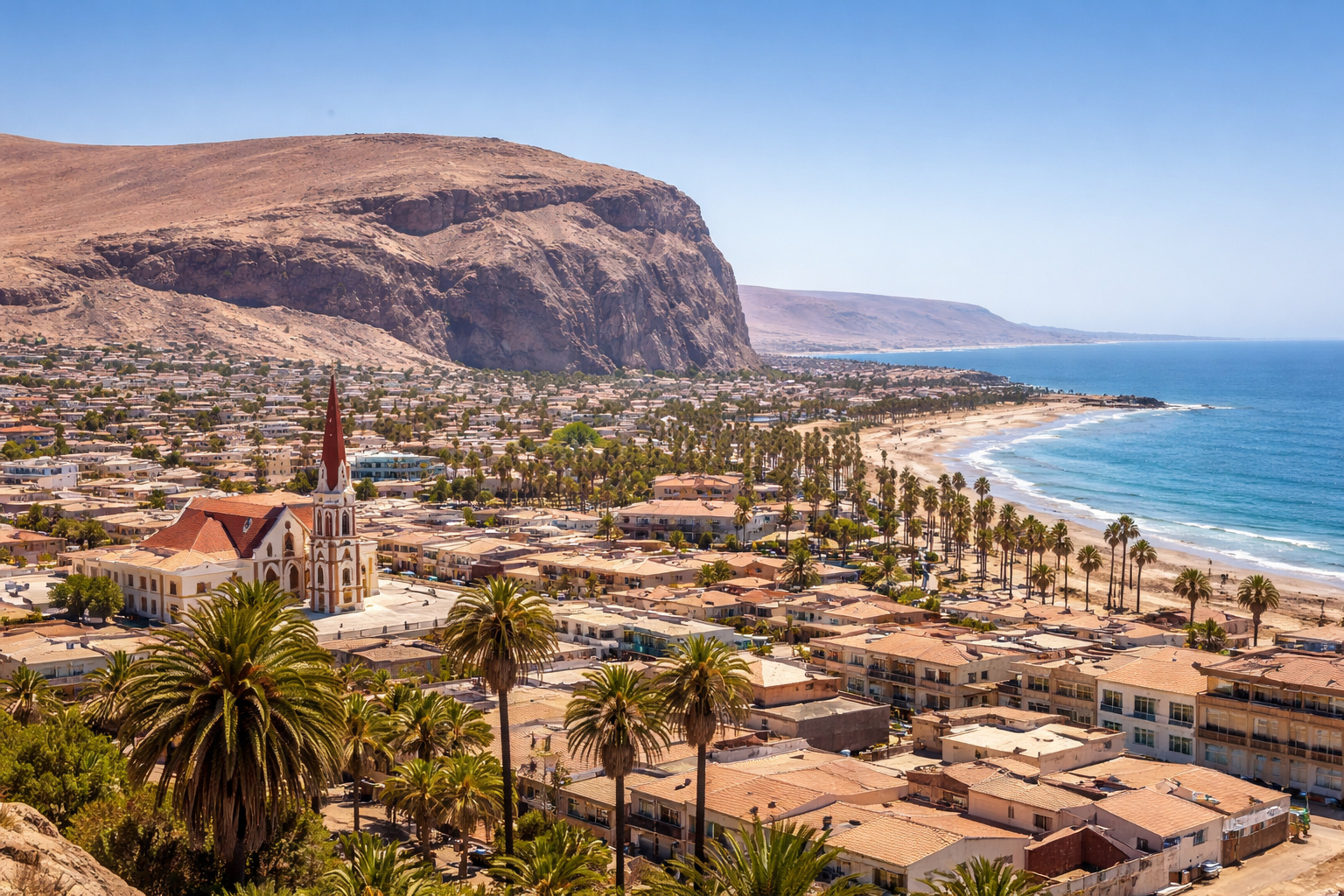 Vista panorâmica de Arica, no Chile, com oceano Pacífico, palmeiras e montanhas do Deserto do Atacama sob céu azul sem nuvens.
