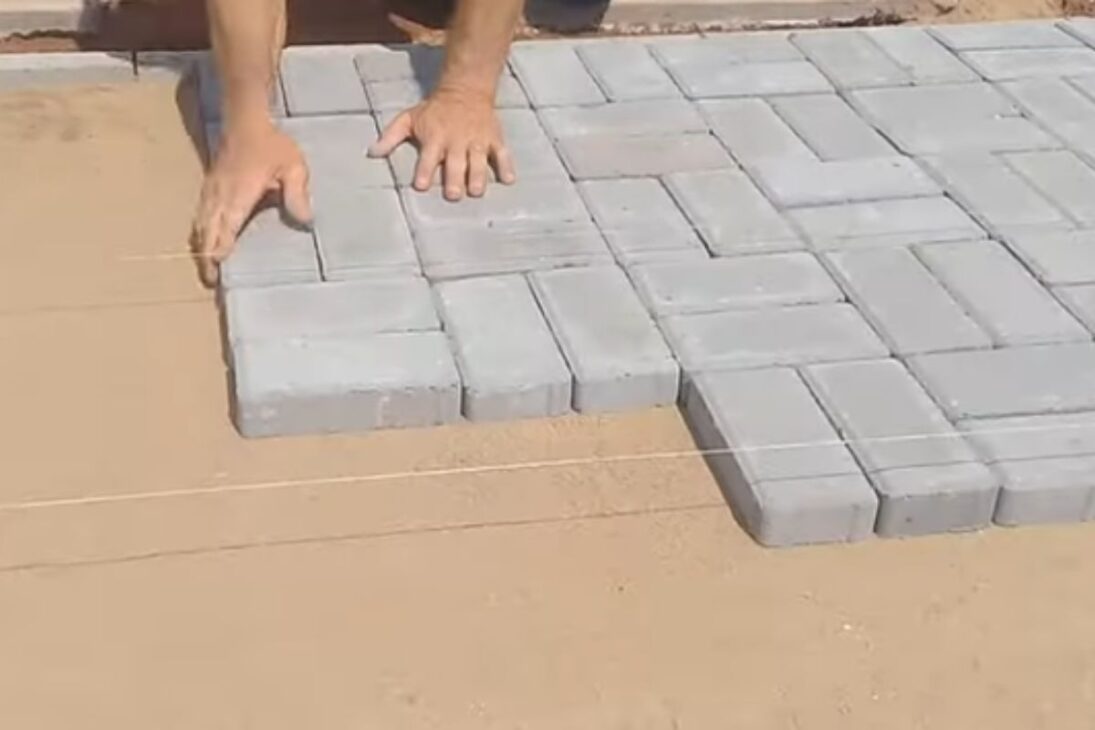 Mason shows interlocking block on the sidewalk with sand and vibratory plate to lock joints and finish.